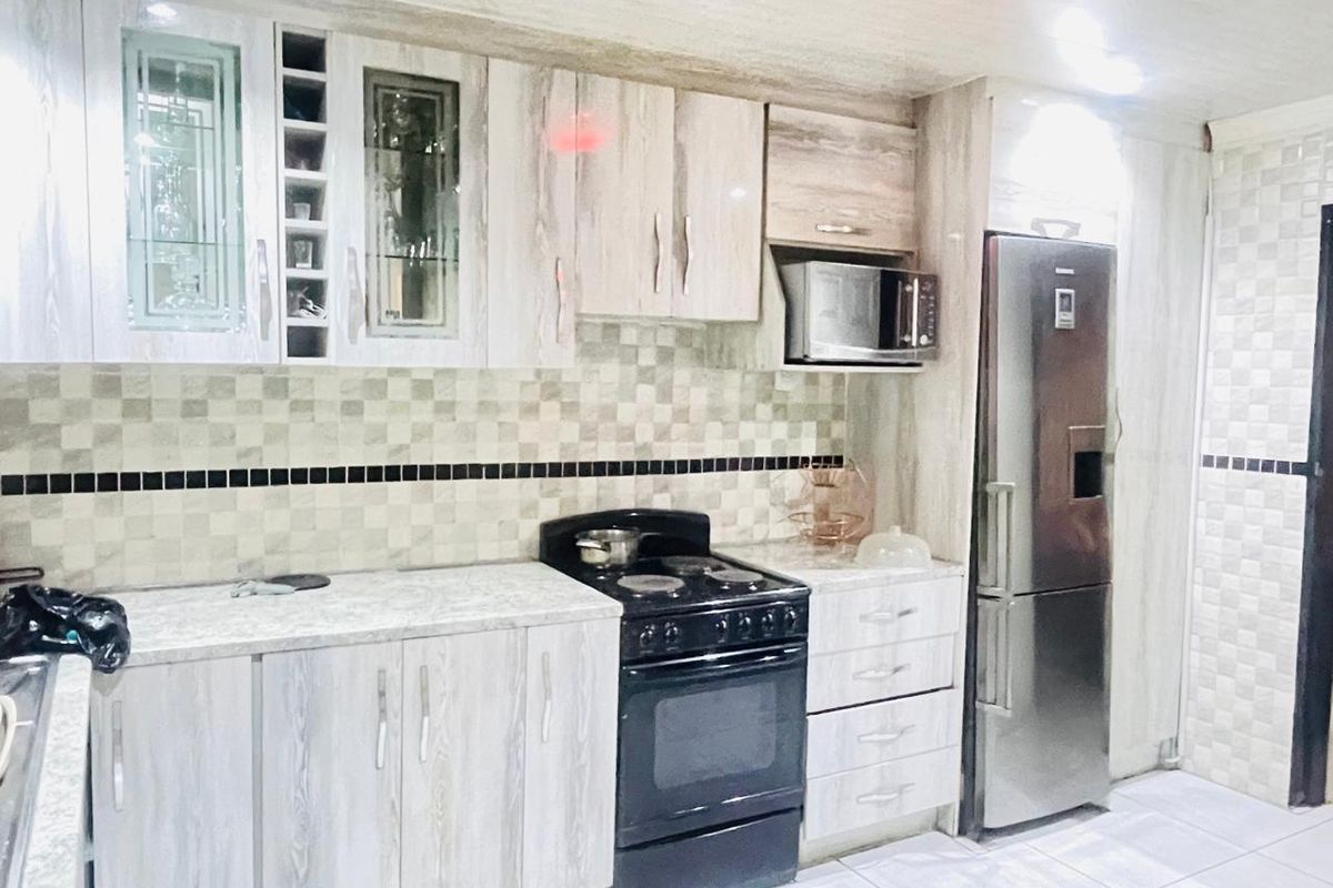 A functional kitchen featuring light wood-grain cabinetry, a tiled backsplash, a built-in microwave, and a freestanding stove.