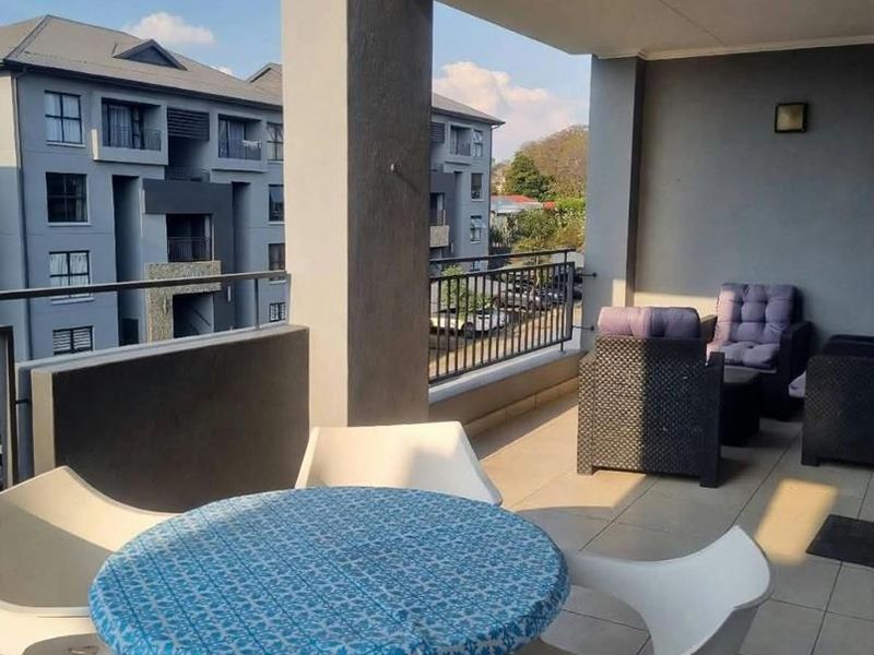 A spacious covered balcony featuring tiled flooring, metal railings, and recessed wall lighting, offering a pleasant outdoor area for relaxation.