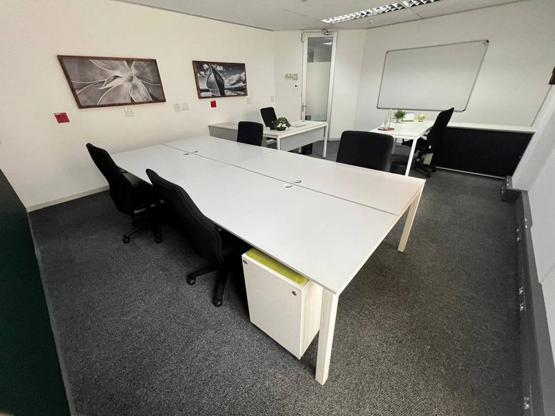 A professional office space featuring carpeted flooring, recessed ceiling lighting, and a wall-mounted whiteboard, providing a functional work environment.