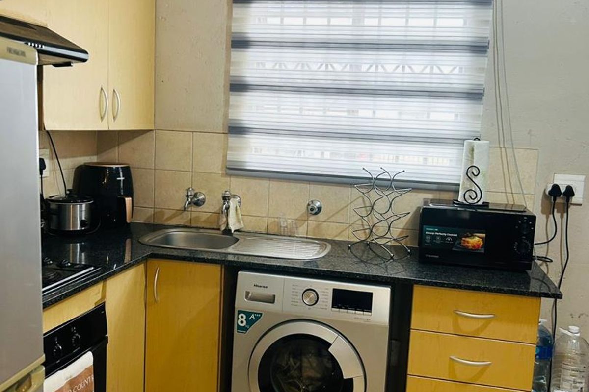 Compact kitchen featuring light wood cabinetry, granite-look countertops, integrated sink, and space for a washing machine.