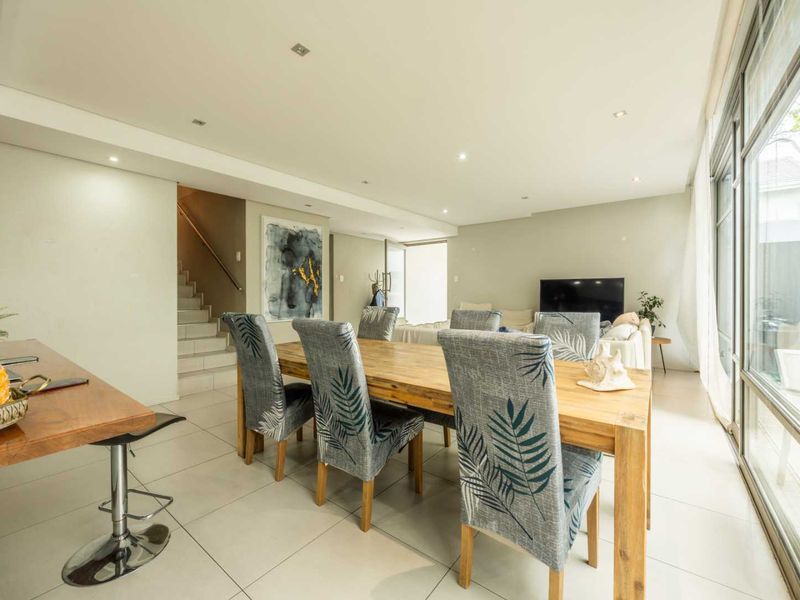 Spacious open-plan living and dining area featuring large sliding glass doors, tiled flooring, and a staircase leading to the upper level.