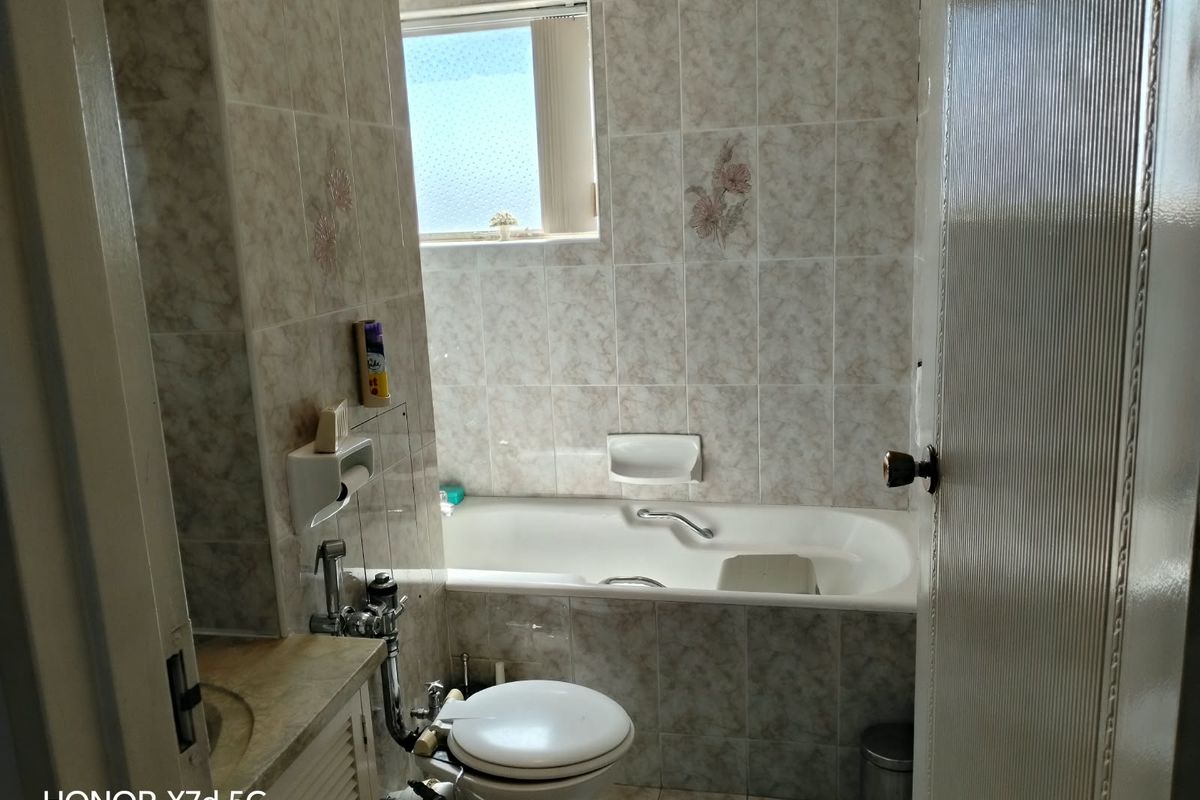 A functional bathroom featuring a built-in bathtub, vanity basin, and toilet, finished with dated ceramic wall tiles and an obscured glass window.