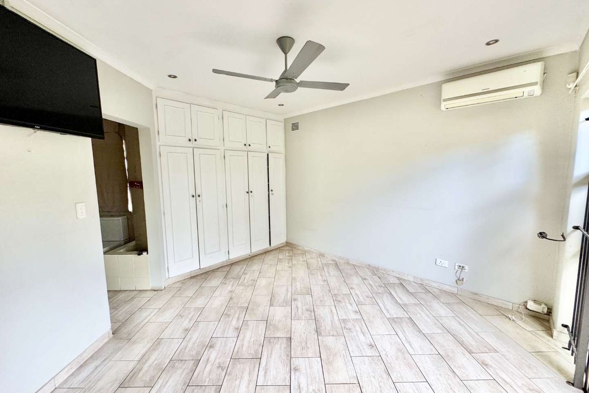Spacious bedroom featuring light-toned tiled flooring, extensive built-in cabinetry, a ceiling fan, and a wall-mounted air conditioning unit.