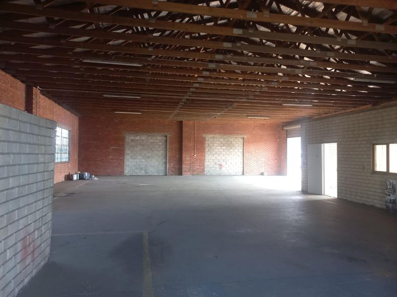 Spacious industrial warehouse unit featuring exposed timber roof trusses, brick walls, concrete flooring, and large access points suitable for various commercial or storage uses.