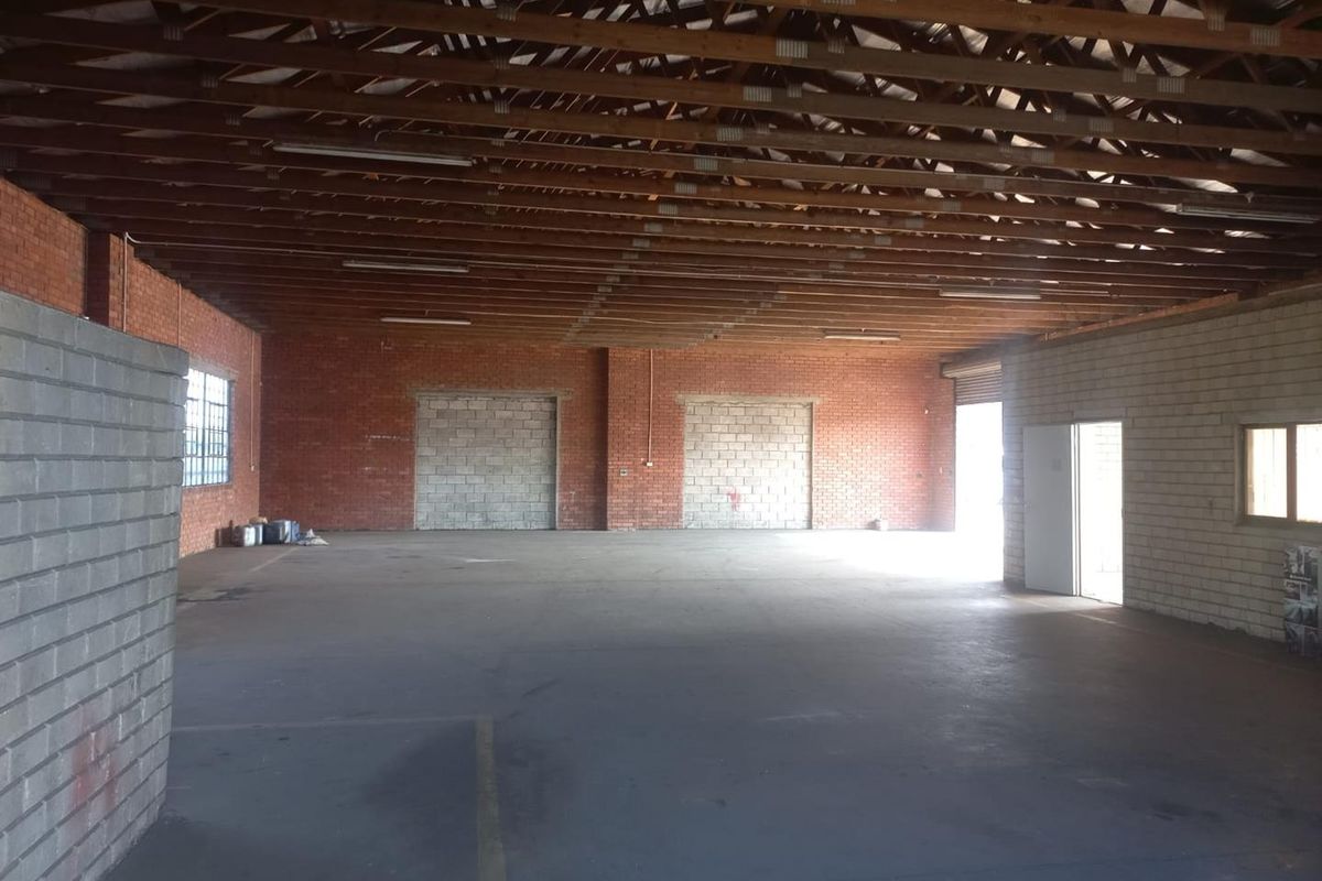 Spacious industrial warehouse unit featuring exposed timber roof trusses, brick walls, concrete flooring, and large access points suitable for various commercial or storage uses.