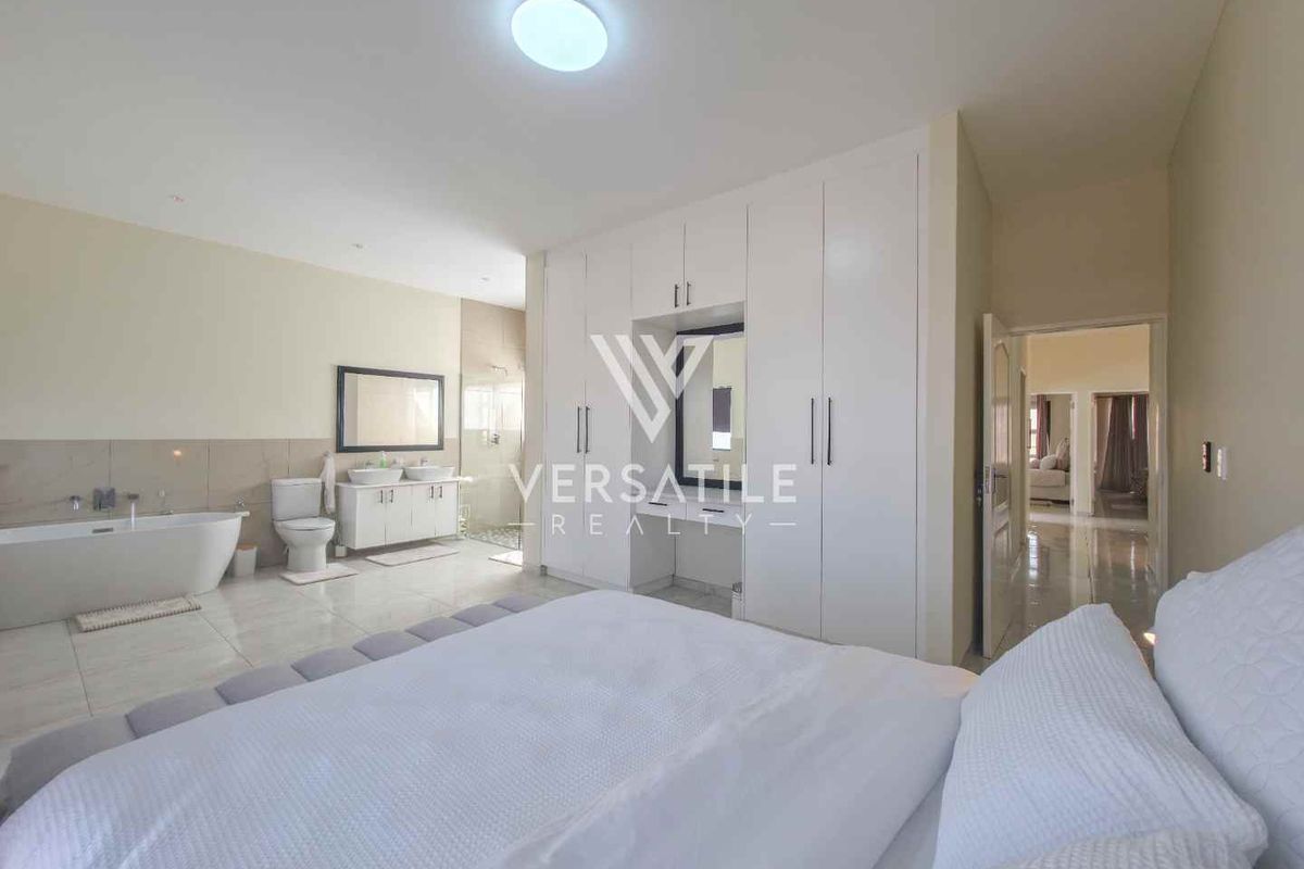 Spacious bedroom featuring an open-plan en-suite bathroom with a freestanding bathtub, double vanity, and extensive built-in cupboard storage.