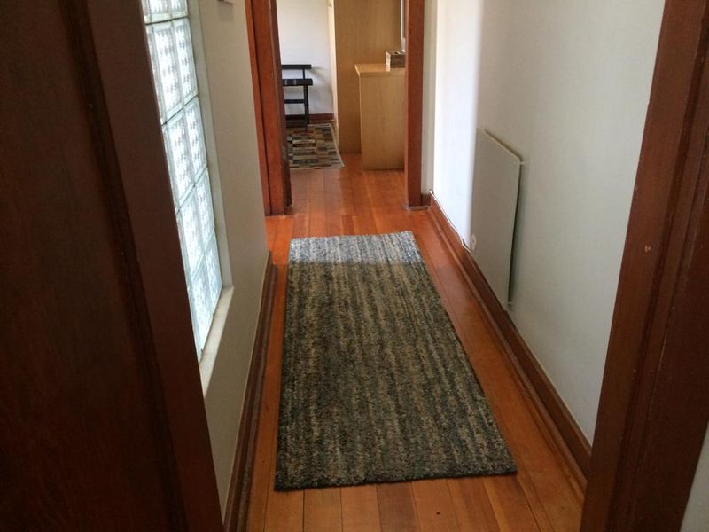 A narrow hallway featuring hardwood flooring, a glass block window for natural light, and a wall-mounted electric heater.