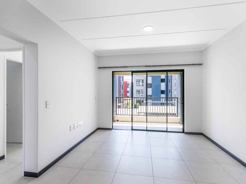 A bright, empty living room featuring neutral tiled flooring and a large sliding glass door that opens onto a private balcony.