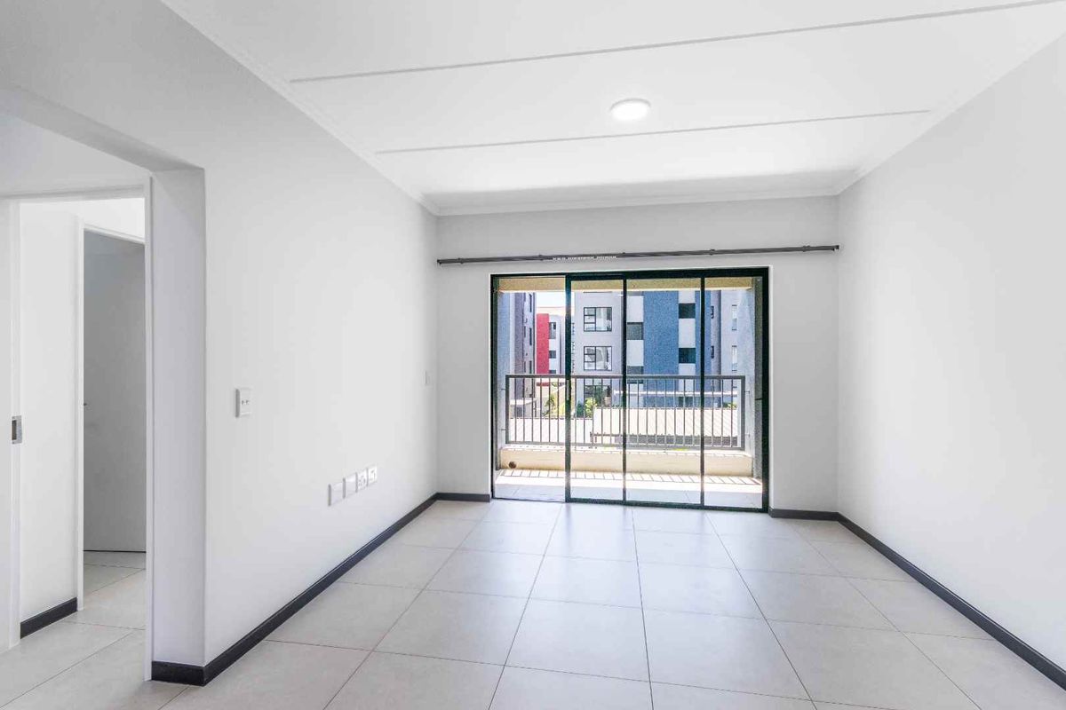 A bright, empty living room featuring neutral tiled flooring and a large sliding glass door that opens onto a private balcony.