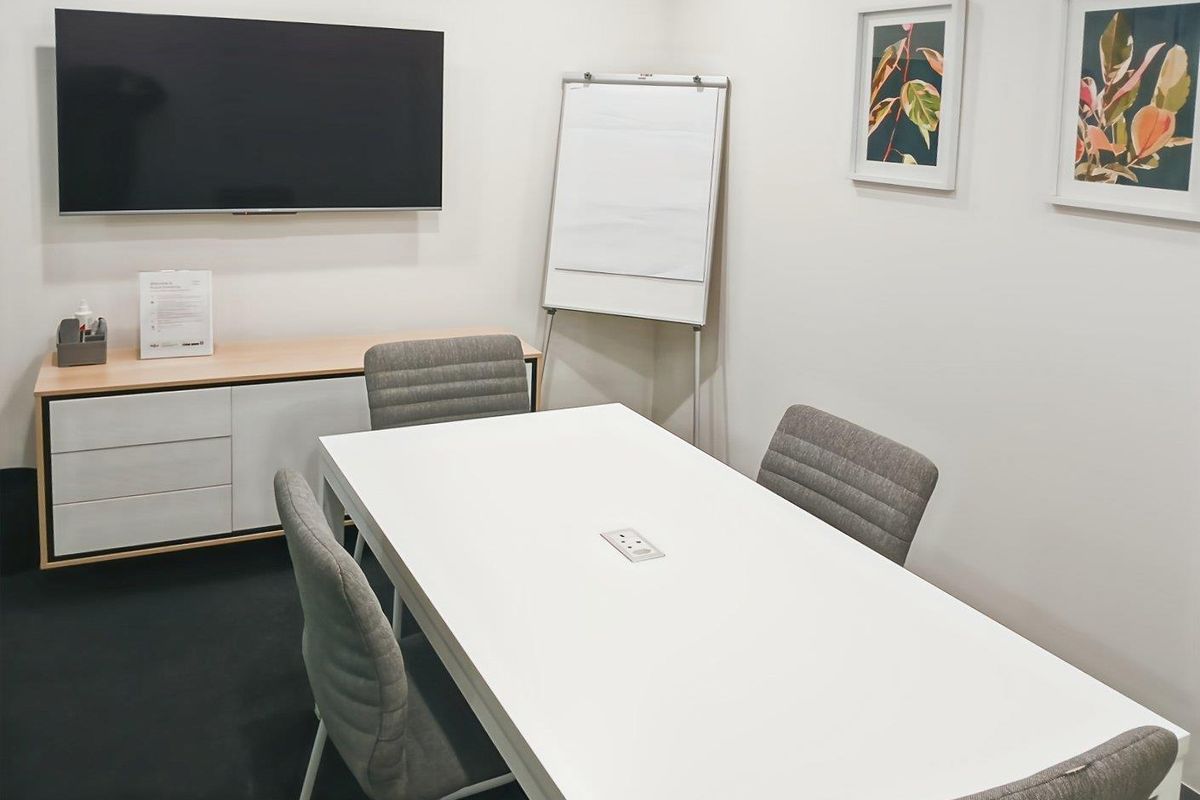 A modern, well-maintained office meeting room featuring a wall-mounted display, built-in storage cabinetry, and integrated desk power connectivity.