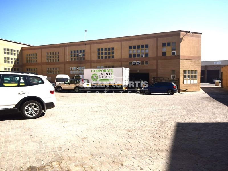 Exterior view of an industrial property featuring a large paved yard and multi-level building facade with numerous windows.