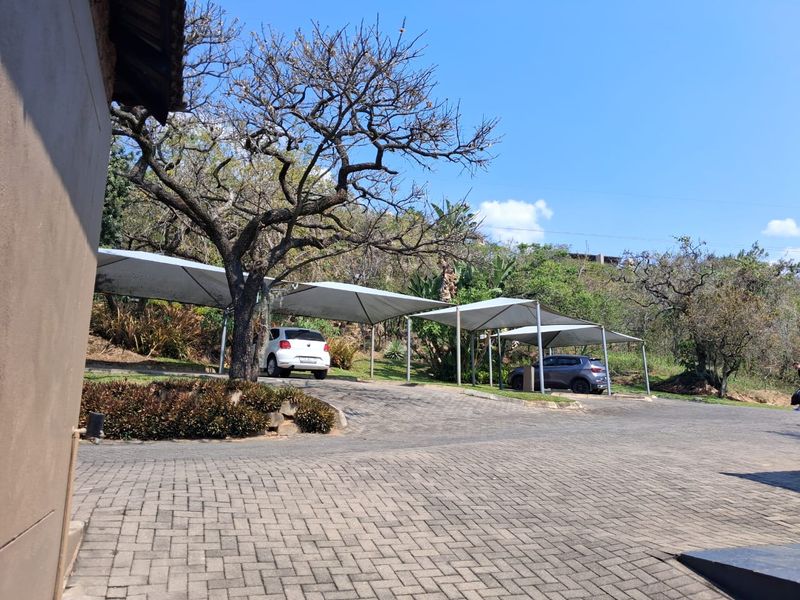 Outdoor parking area featuring paved driveway and multiple shade cloth carports set within a landscaped environment.