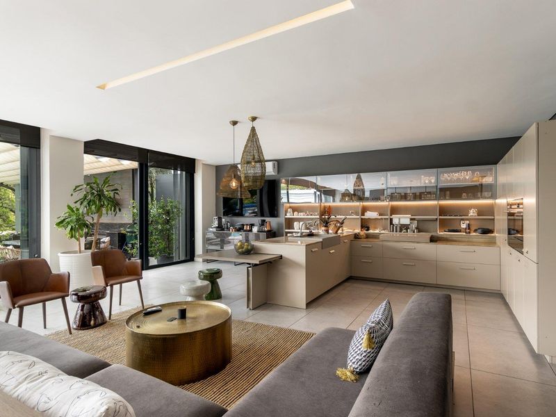 Modern open-plan living and kitchen area featuring sleek built-in cabinetry, a central island, and seamless indoor-outdoor flow through large sliding glass doors.