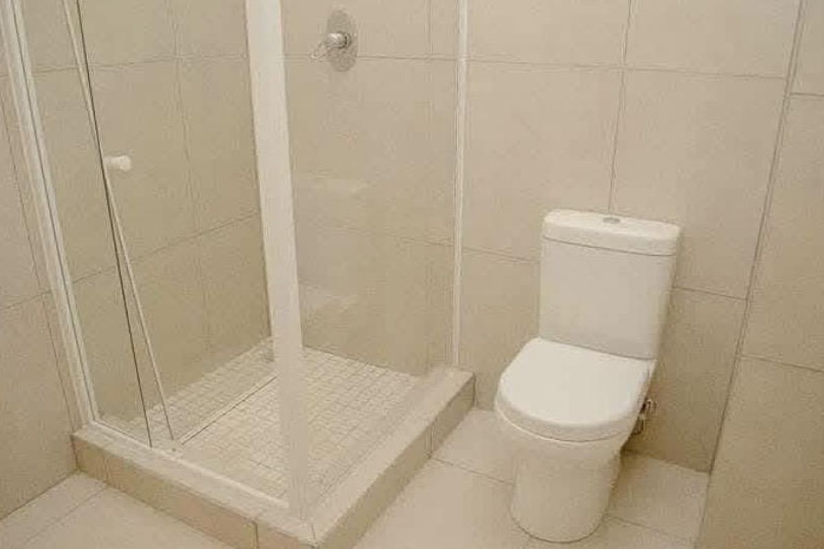 A functional bathroom featuring a glass-enclosed shower and a standard toilet with neutral wall and floor tiling.