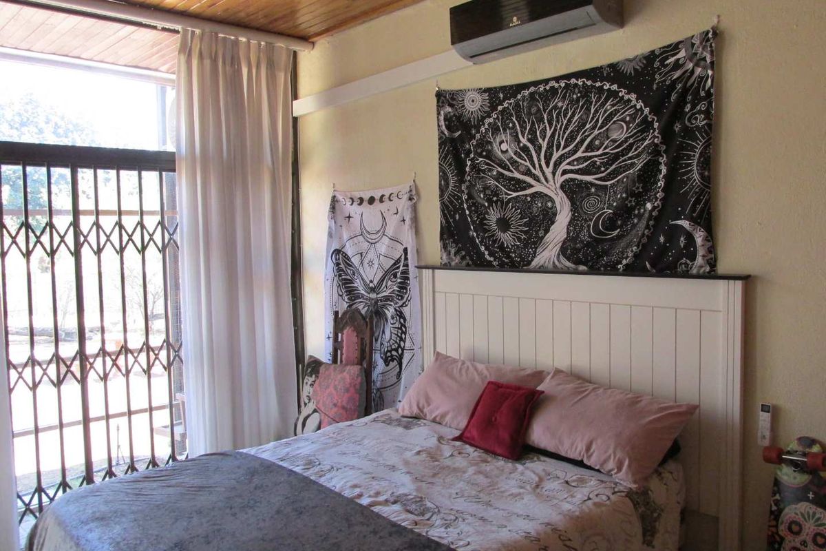A bedroom featuring a timber-paneled ceiling, wall-mounted air conditioning unit, and large sliding glass door with security gate.