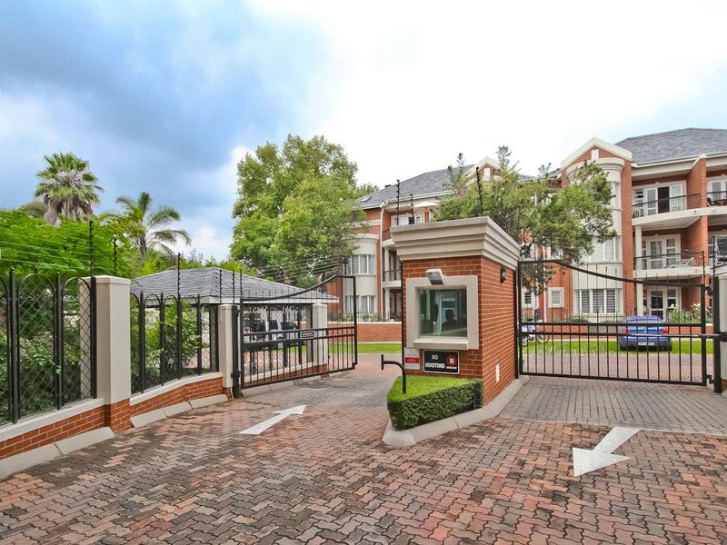Secure gated entrance to the apartment complex featuring a guard house, brick facade, and paved driveway access.