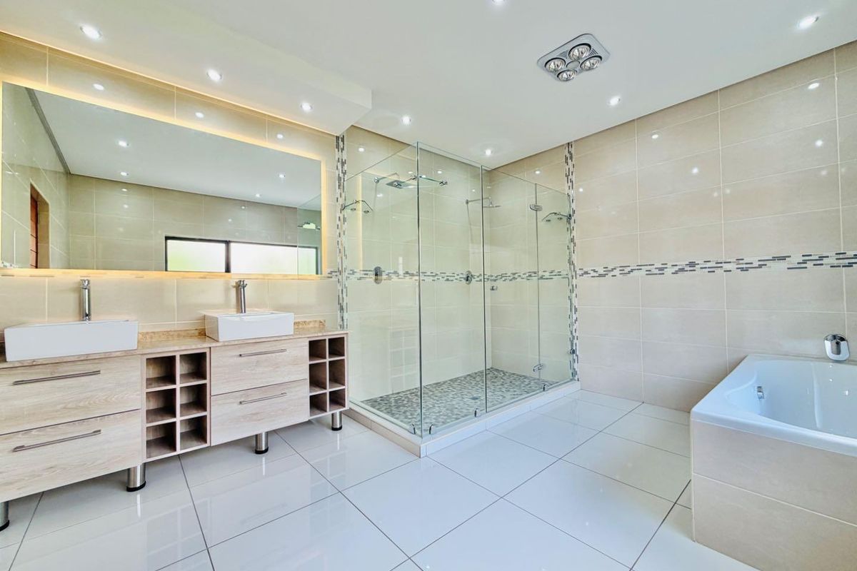 Modern, spacious bathroom featuring a double vanity with vessel sinks, a large glass-enclosed walk-in shower, and a built-in bathtub with neutral tiled finishes.