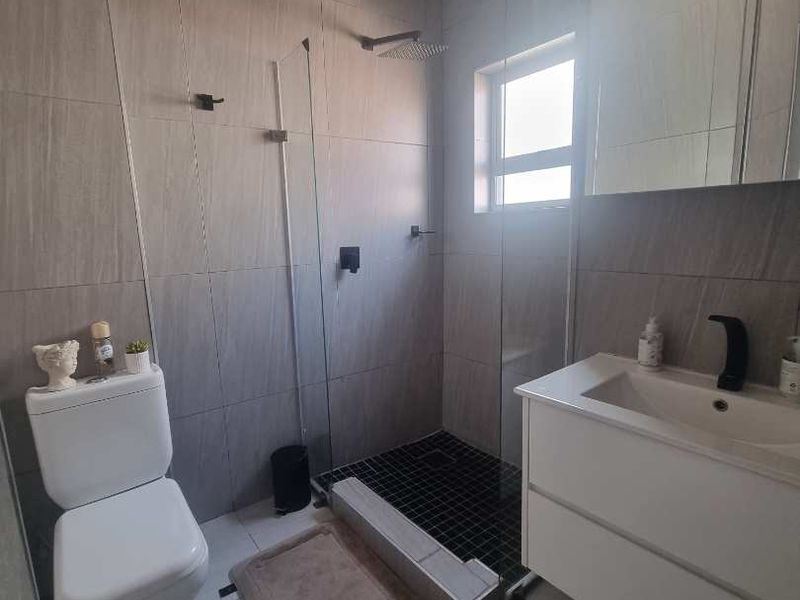 Modern bathroom featuring a walk-in shower with a rain shower head, wall-mounted vanity, and contemporary grey wall tiling.