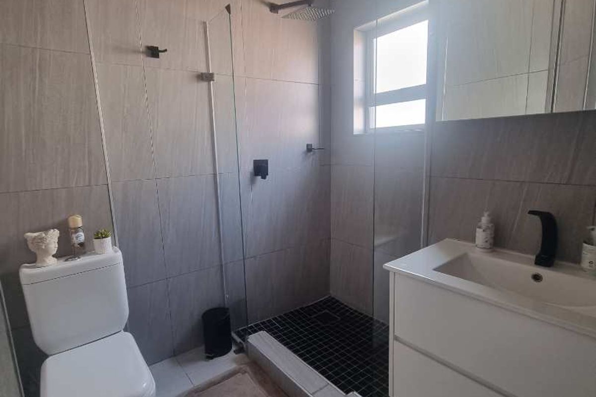 Modern bathroom featuring a walk-in shower with a rain shower head, wall-mounted vanity, and contemporary grey wall tiling.