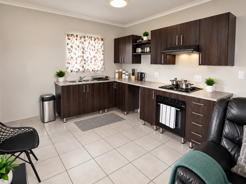 Open-plan kitchen featuring dark wood cabinetry, laminate countertops, built-in oven, gas hob, and tiled flooring, seamlessly integrated into the living space.