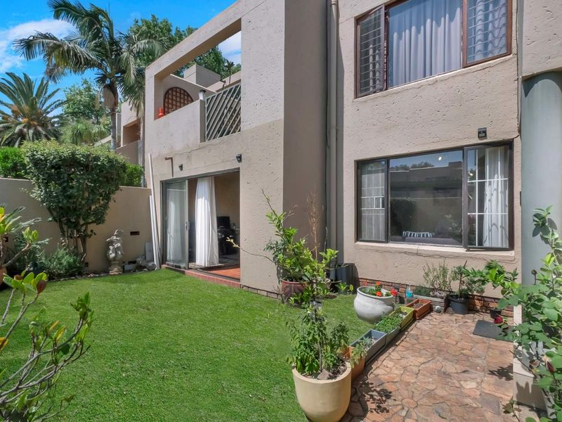 Rear view of the apartment featuring a private garden, stone paved patio, and an upper-level balcony with sliding door access.