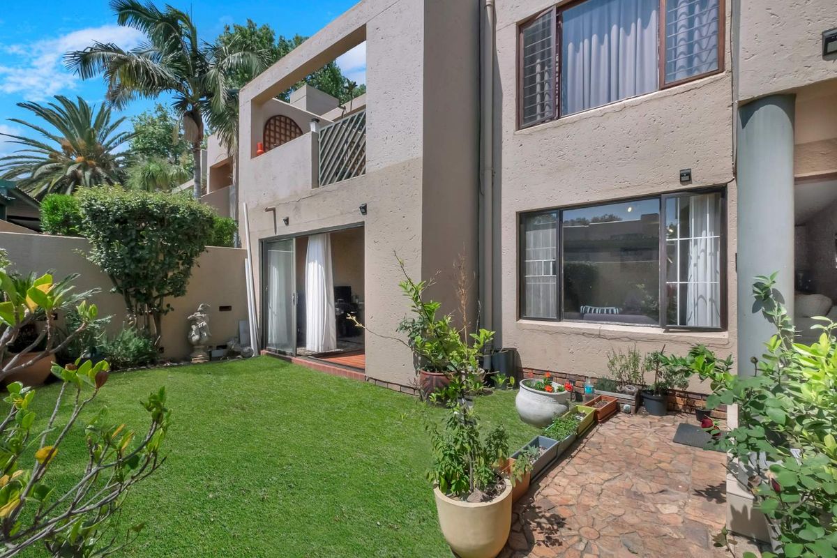 Rear view of the apartment featuring a private garden, stone paved patio, and an upper-level balcony with sliding door access.