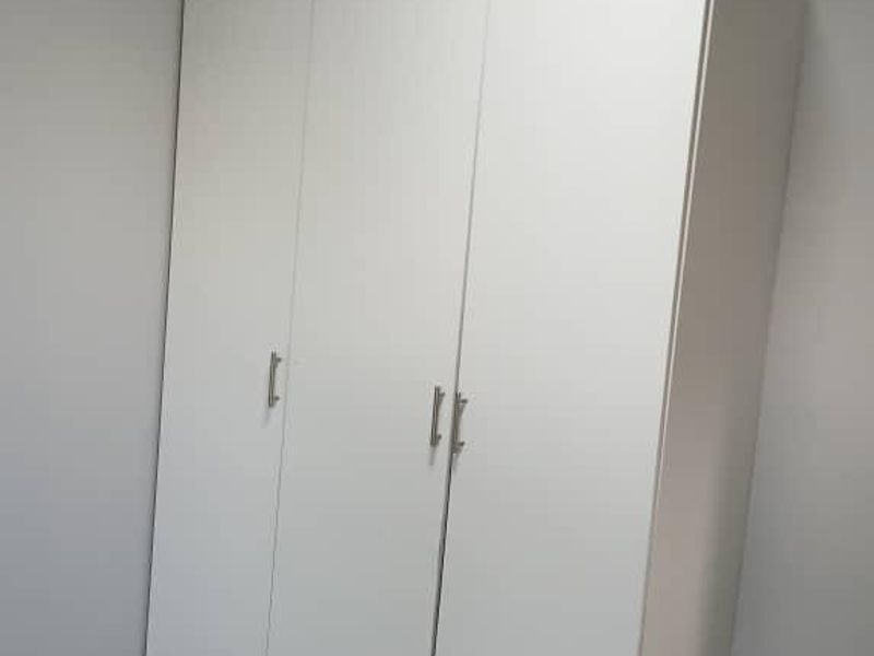 A clean, empty bedroom featuring modern grey floor tiles and a white built-in wardrobe with silver handles.