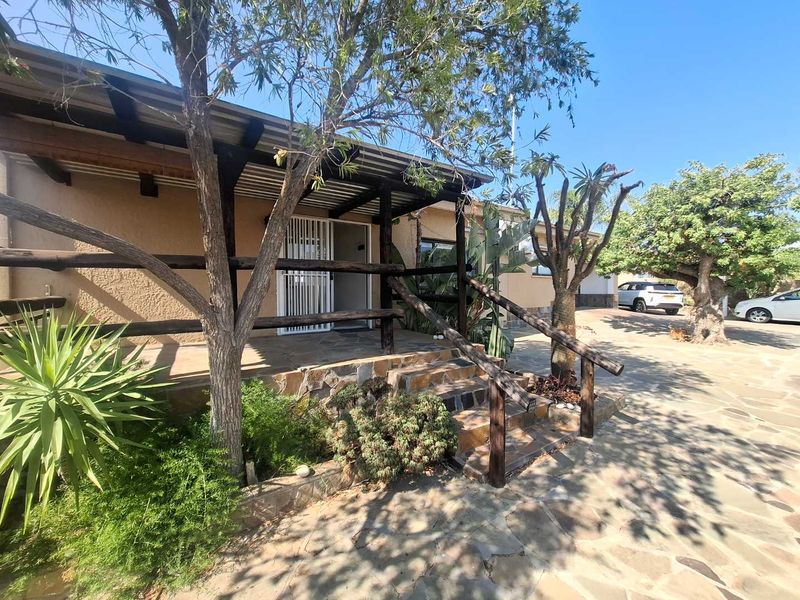 Front entrance featuring a covered patio with timber railings, stone cladding, and stone paved driveway area.