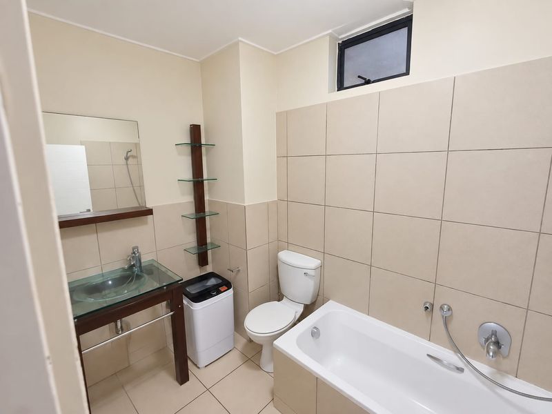 A functional bathroom featuring a glass vessel sink, built-in bathtub with chrome fixtures, tiled walls, and a small frosted window for natural light.
