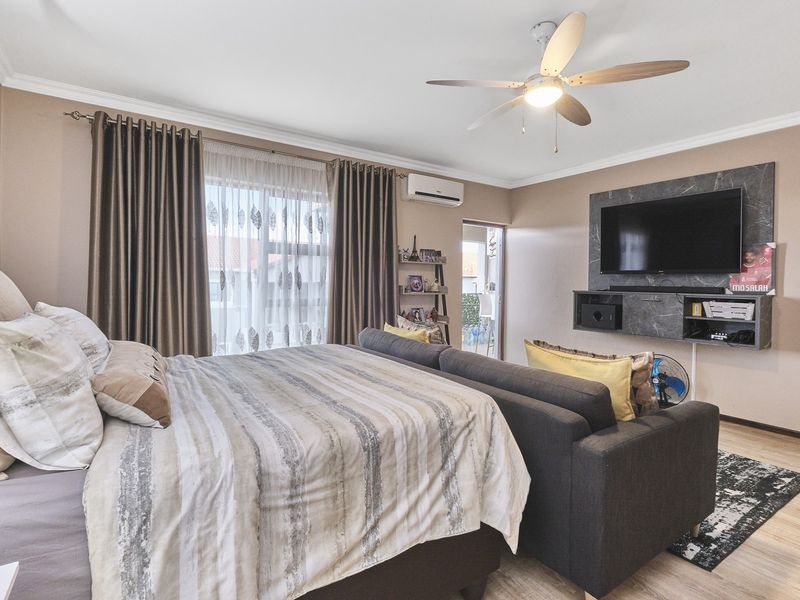 Spacious bedroom featuring a ceiling fan, split-system air conditioning, and a modern built-in media console with laminate flooring throughout.