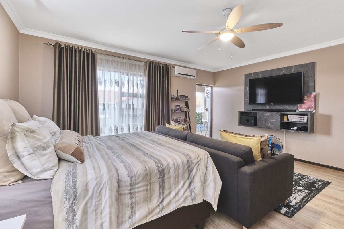 Spacious bedroom featuring a ceiling fan, split-system air conditioning, and a modern built-in media console with laminate flooring throughout.