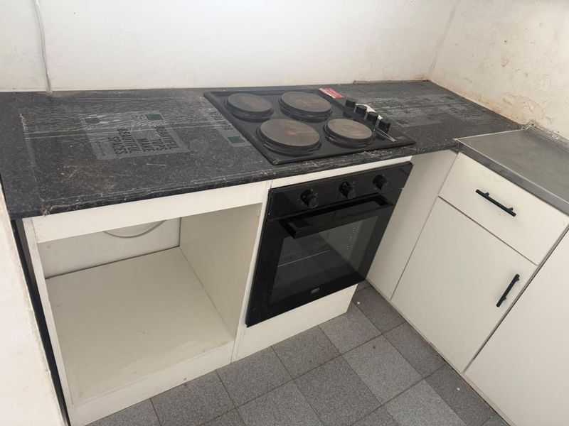 A compact kitchen area featuring a built-in oven, electric hob, laminate countertops, and base cabinetry, currently requiring minor wall repairs and finishing touches.