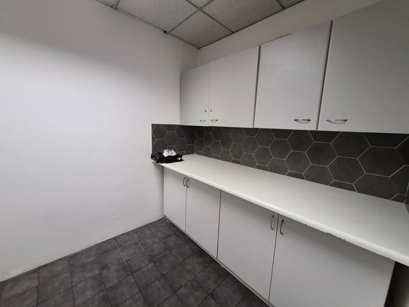 A functional kitchenette area featuring white built-in cabinetry, a modern hexagonal tile backsplash, and durable tiled flooring.