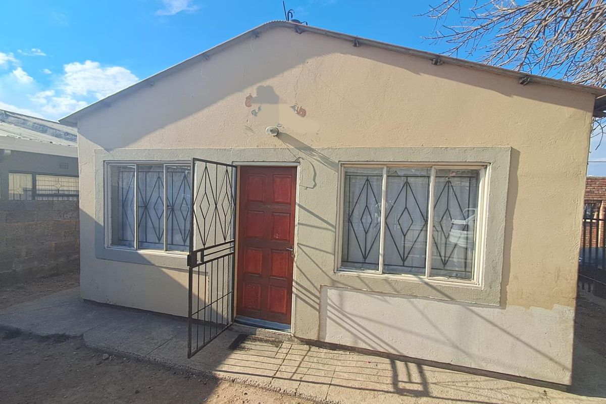 Front elevation of a single-story house featuring a timber entrance door, security gate, and aluminium-framed windows with visible exterior wall wear.