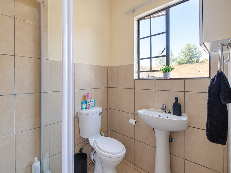 A functional bathroom featuring a pedestal sink, toilet, and a shower enclosure with neutral wall tiling and natural light from the window.