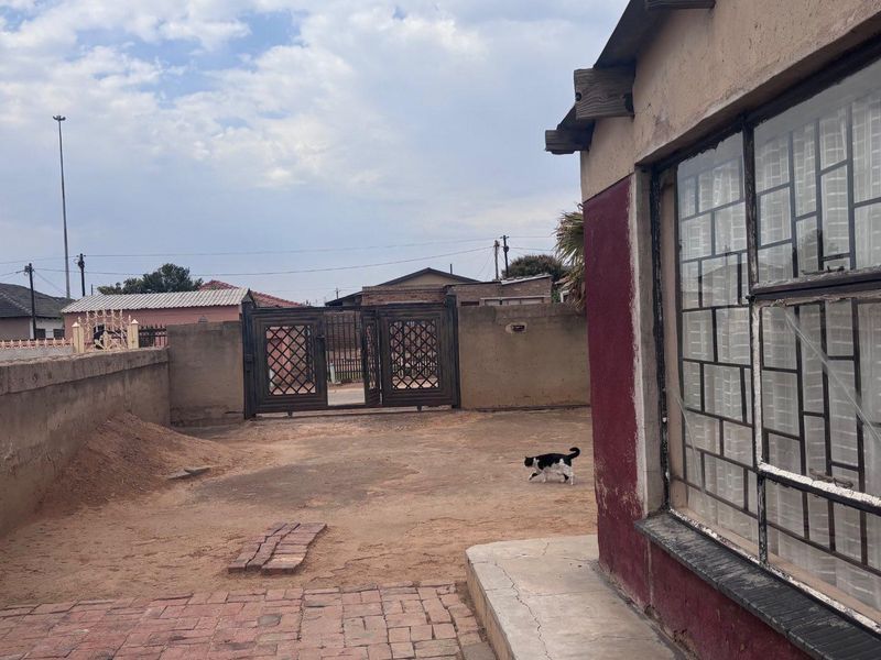 Rear exterior view of the property featuring a perimeter wall, metal security gate, and paved walkway with visible wear to the exterior finishes.