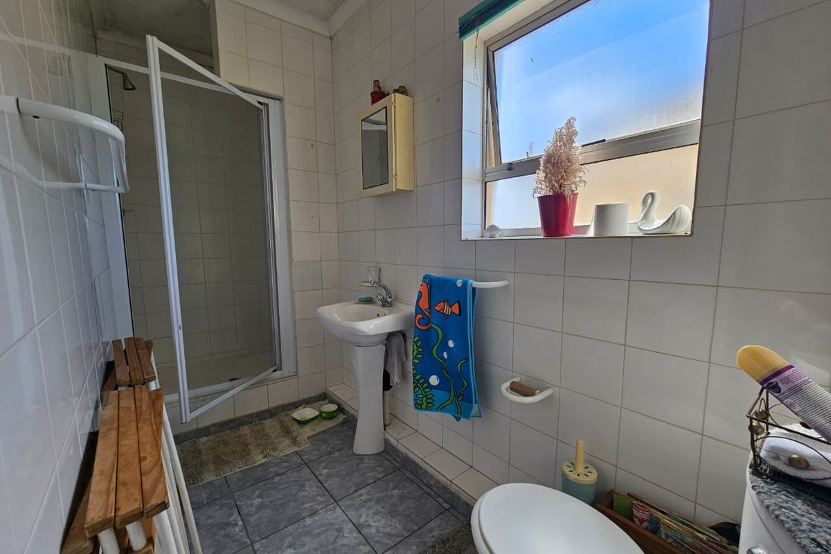 A functional bathroom featuring a pedestal basin, a shower enclosure with a glass door, and tiled walls and flooring.