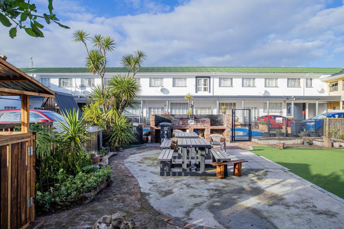 A communal outdoor courtyard area featuring a built-in brick braai, paved and artificial grass sections, and access to the apartment complex units.