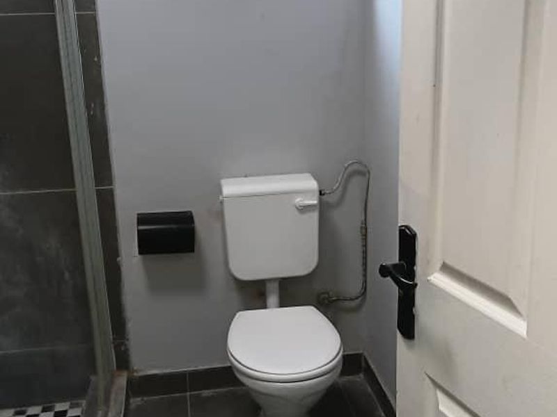 A compact bathroom featuring a shower enclosure, toilet, and tiled flooring with a small window for natural light.