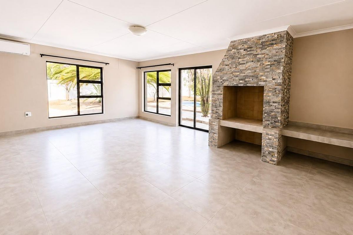 Spacious living area featuring a prominent stone-clad fireplace, neutral tiled flooring, split-system air conditioning, and large windows providing natural light and garden views.