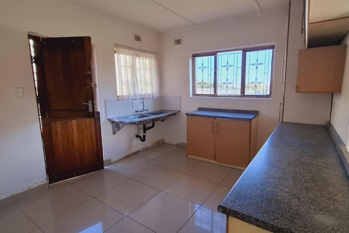 An empty kitchen featuring tiled floors, laminate countertops, a stainless steel sink, and built-in cabinetry, requiring cosmetic updates to improve its condition.