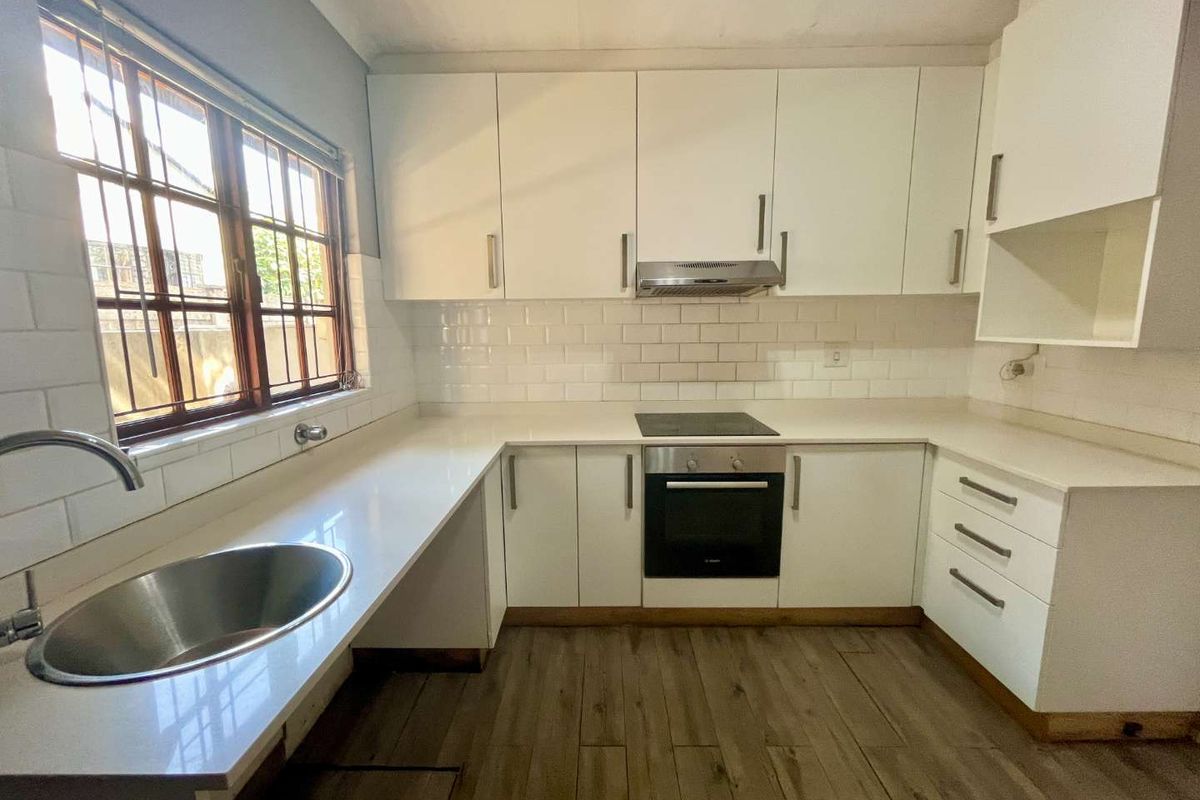 Modern kitchen featuring white cabinetry, subway tile backsplash, stone countertops, integrated oven, hob, extractor fan, and a stainless steel sink.