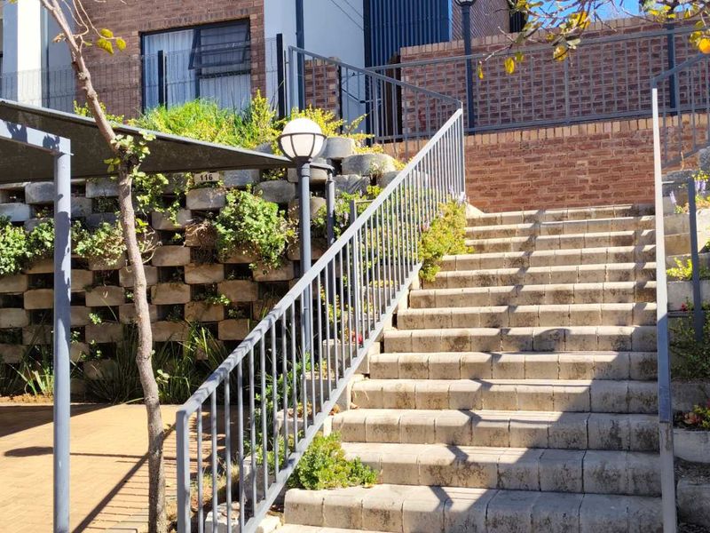 Exterior view of a residential apartment complex featuring a paved driveway, concrete staircase with metal handrails, and landscaped retaining walls.