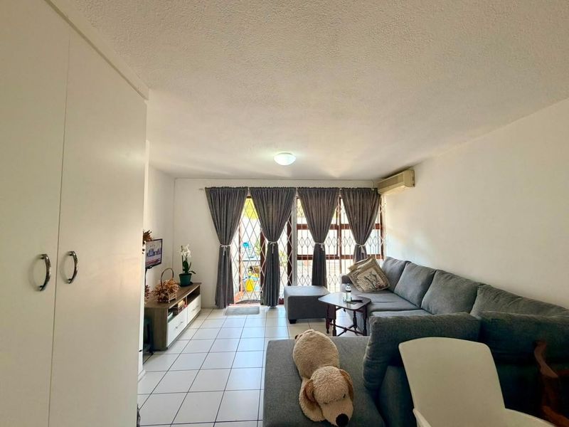 A living room featuring tiled flooring, a built-in cupboard, and an air conditioning unit, with access to an outdoor area through a security gate.