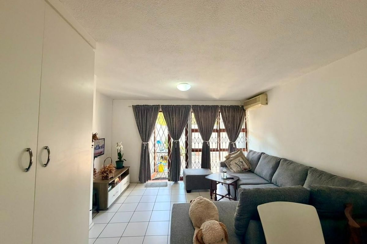 A living room featuring tiled flooring, a built-in cupboard, and an air conditioning unit, with access to an outdoor area through a security gate.