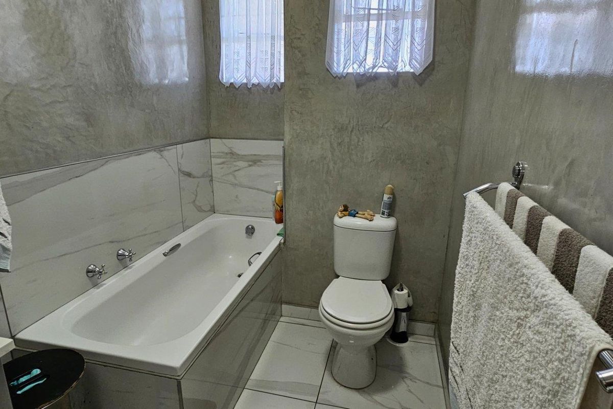 Modern bathroom featuring a built-in bathtub, toilet, and contemporary tiled finishes with a stylish cement-look wall treatment.