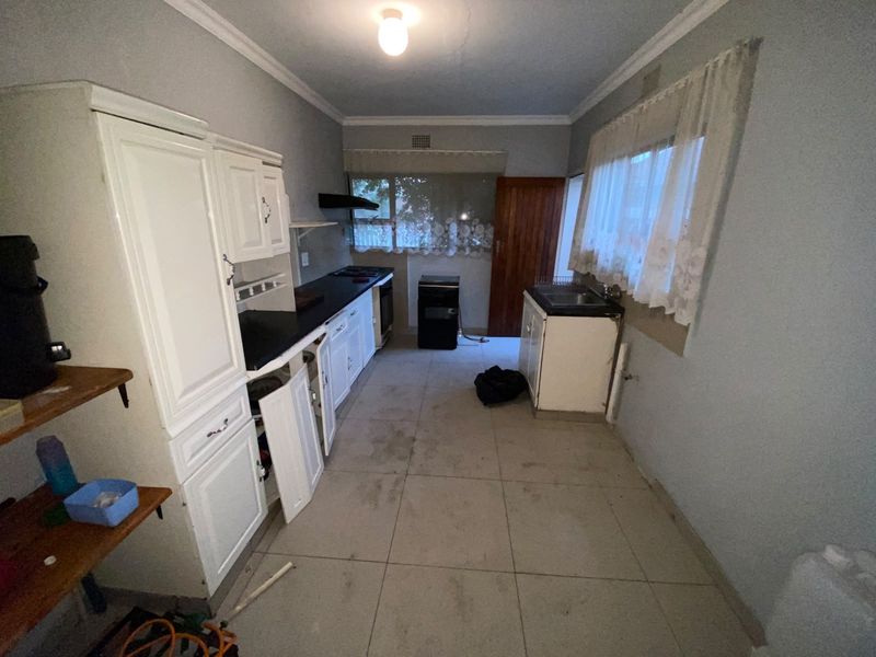 A dated kitchen featuring built-in cabinetry, tiled flooring, and an extractor fan, currently in need of renovation and cosmetic updates.