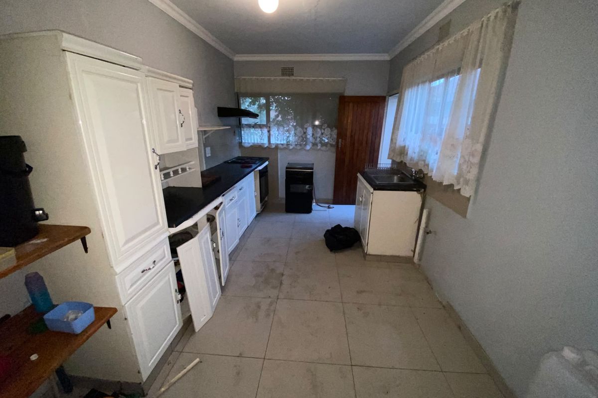 A dated kitchen featuring built-in cabinetry, tiled flooring, and an extractor fan, currently in need of renovation and cosmetic updates.