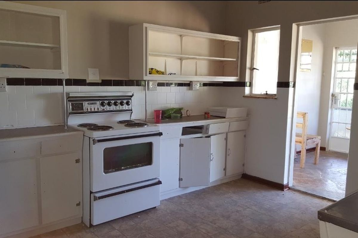 A dated kitchen featuring white cabinetry, a freestanding electric stove, and tiled splashbacks, requiring modernization and repairs to cabinetry and finishes.