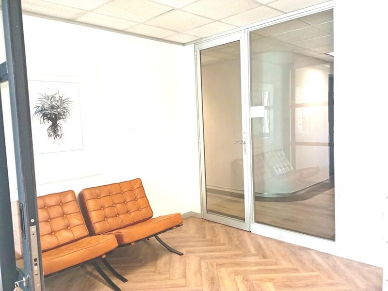 A modern office space featuring a glass partition wall, a glass door, and stylish herringbone flooring, creating a bright and professional work environment.